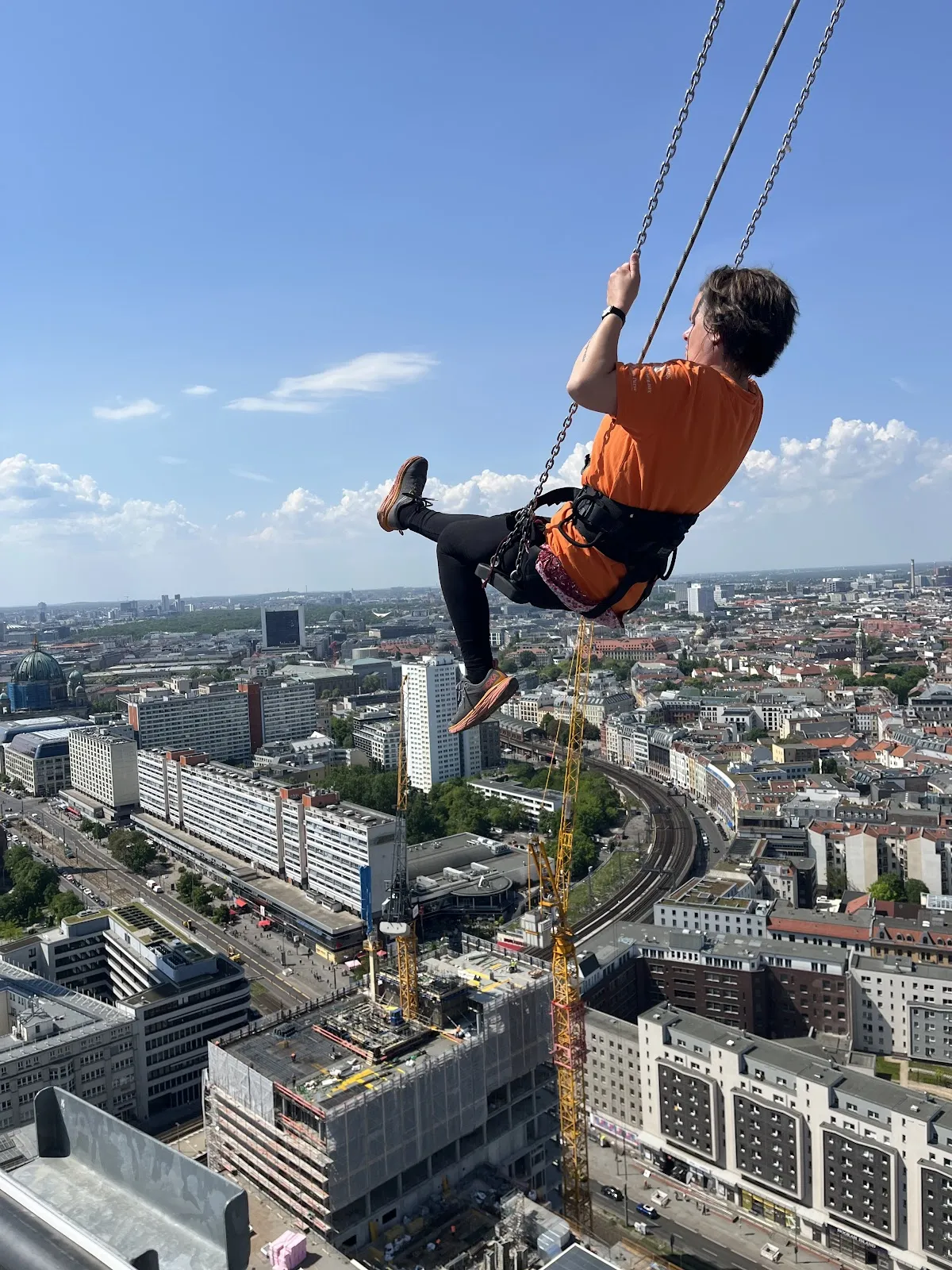 Люди, катающиеся на качелях High Swing Berlin с видом на город