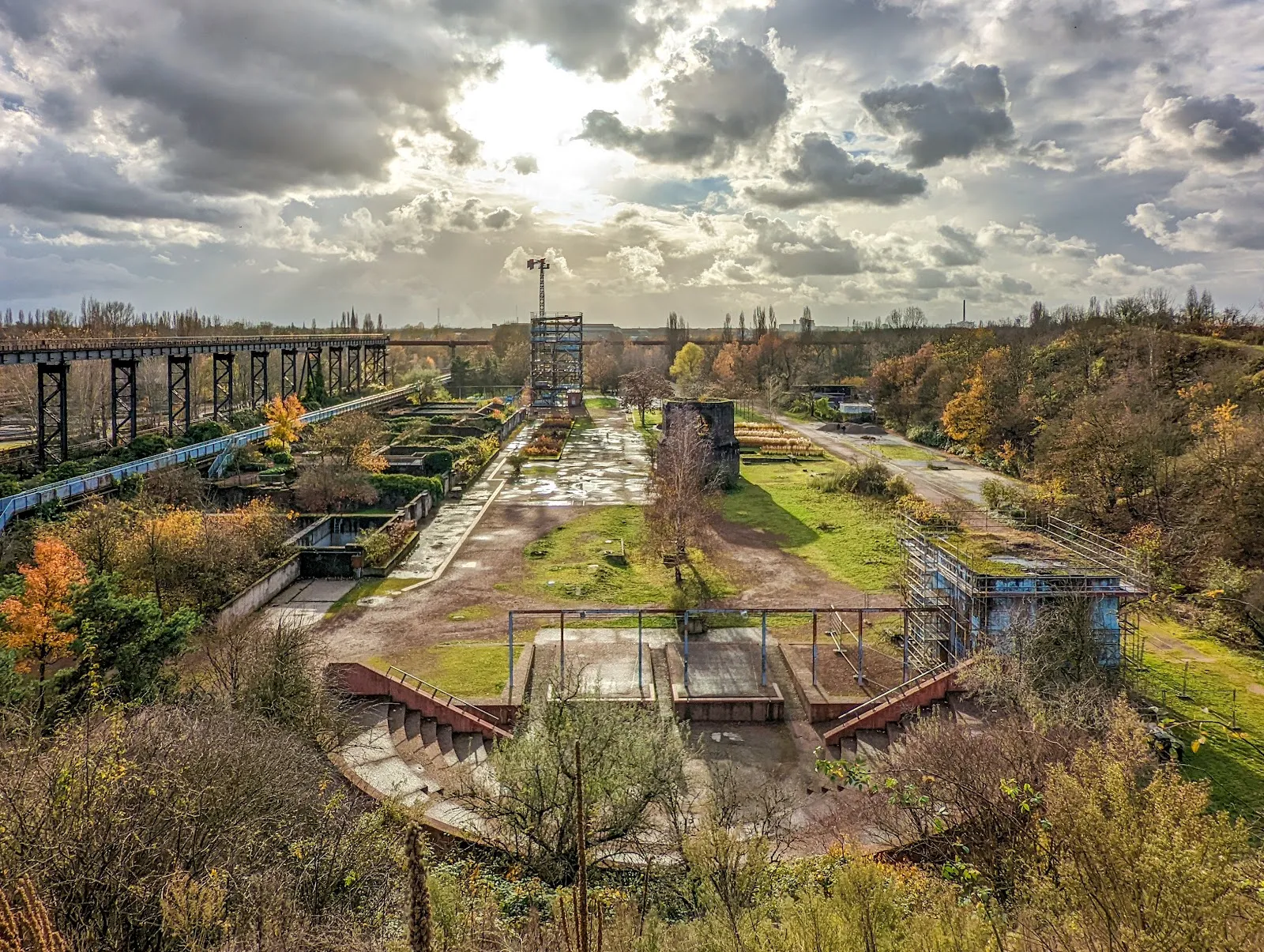 Люди гуляют по Ландшафтному парку Дуйсбург-Норд среди старых промышленных сооружений и зелени.