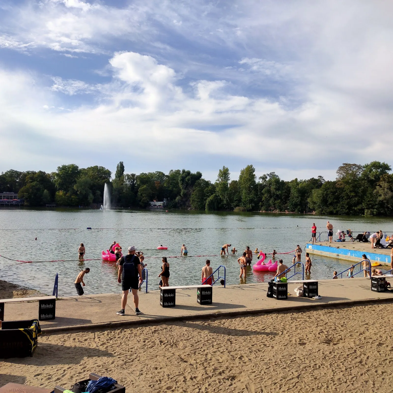 Пляж Вайсензее с людьми, загорающими и купающимися в озере.