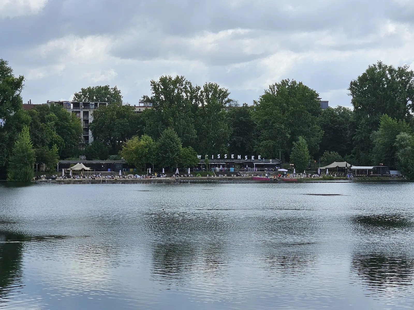 Пляж Вайсензее с людьми, загорающими и купающимися в озере.