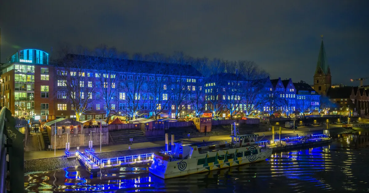 Люди гуляют по набережной Шлахте в Бремене, Германия, с магазинами и кафе.