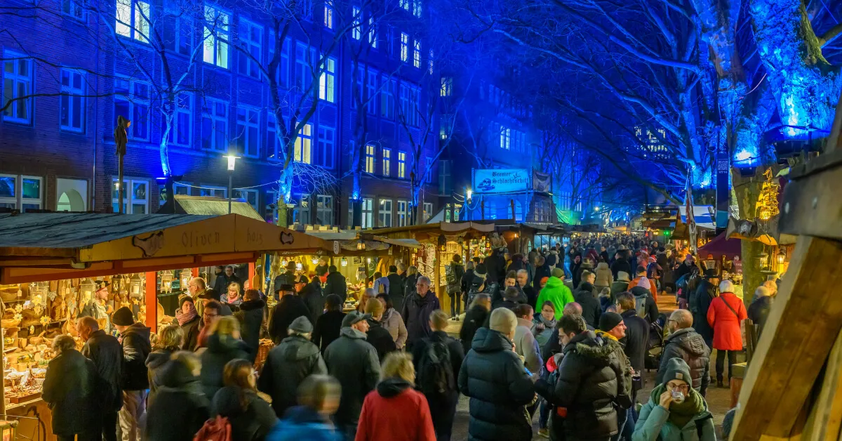 Люди гуляют по набережной Шлахте в Бремене, Германия, с магазинами и кафе.