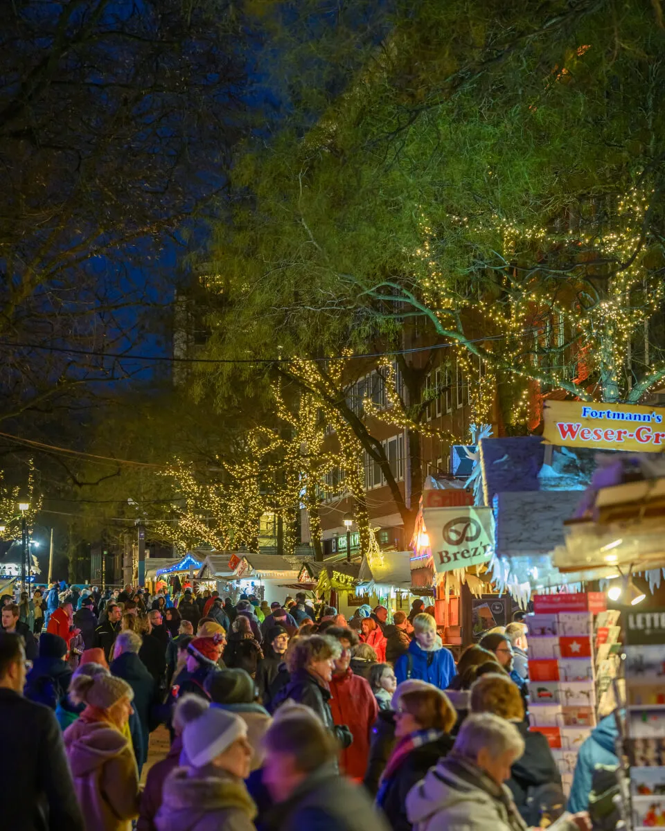 Люди гуляют по набережной Шлахте в Бремене, Германия, с магазинами и кафе.